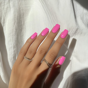 Fuchsia pink gel nail polish applied on manicured nails with silver rings in natural light.
